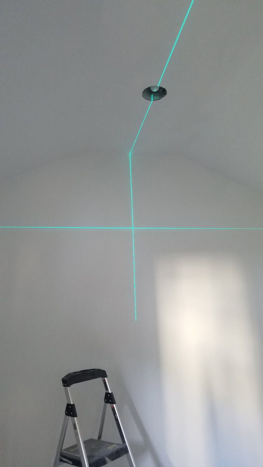 Blue laser lines on a white wall and ceiling, with a step ladder below near a ceiling light fixture.