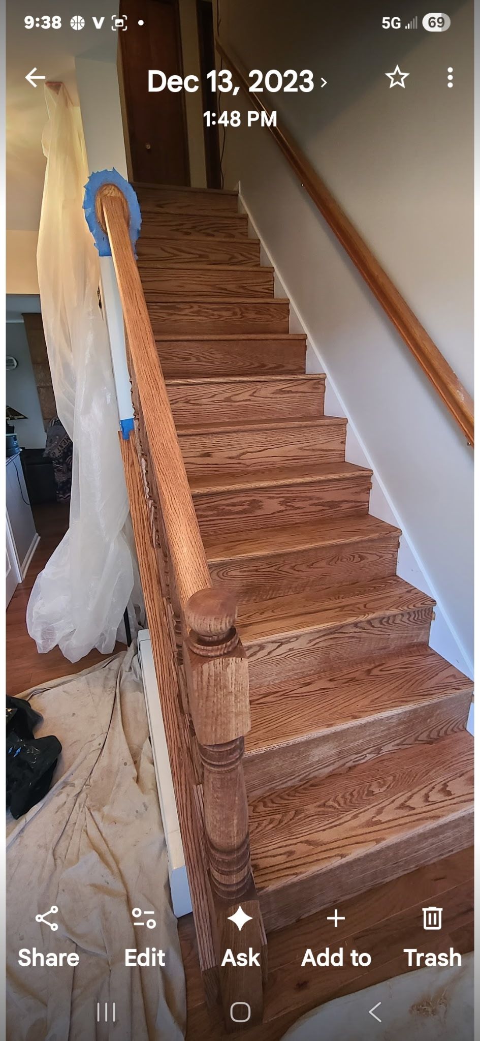 A straight wooden staircase with a banister and decorative newel post, under construction with plastic sheeting.