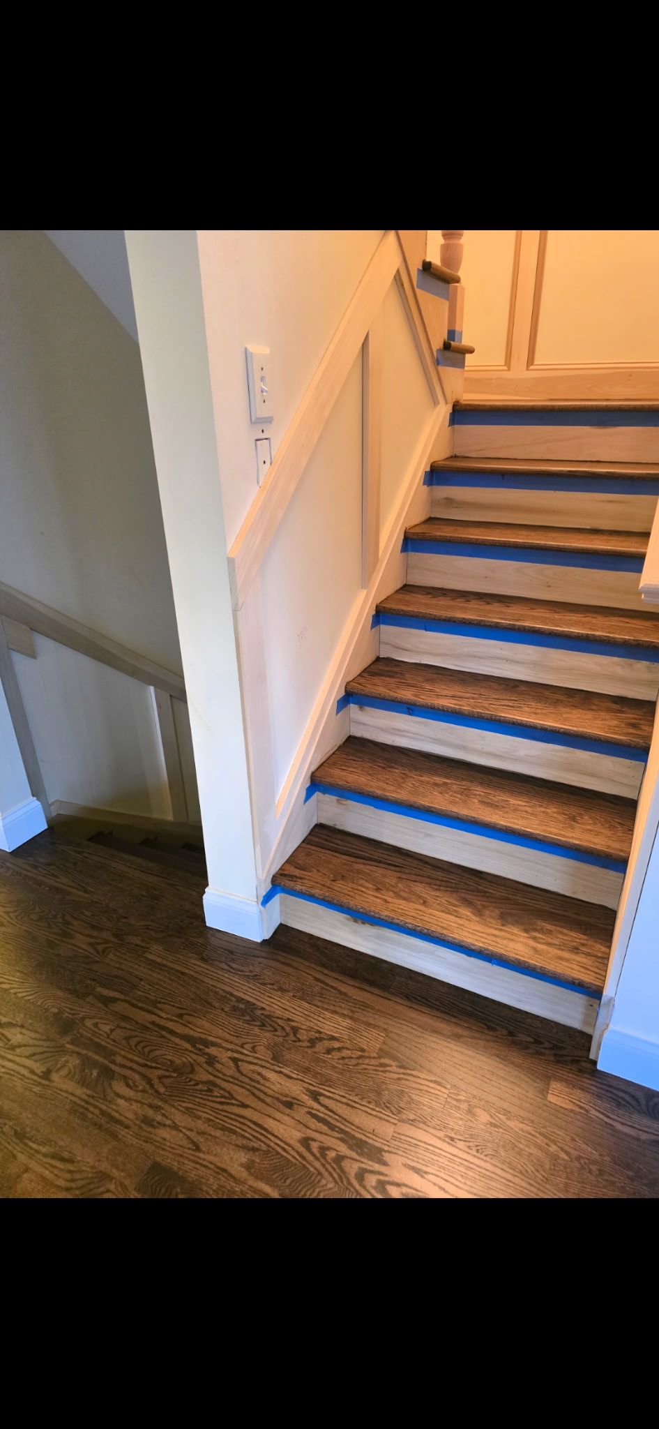 A staircase under renovation with wooden treads covered in blue painter's tape, contrasting with white risers and trim.