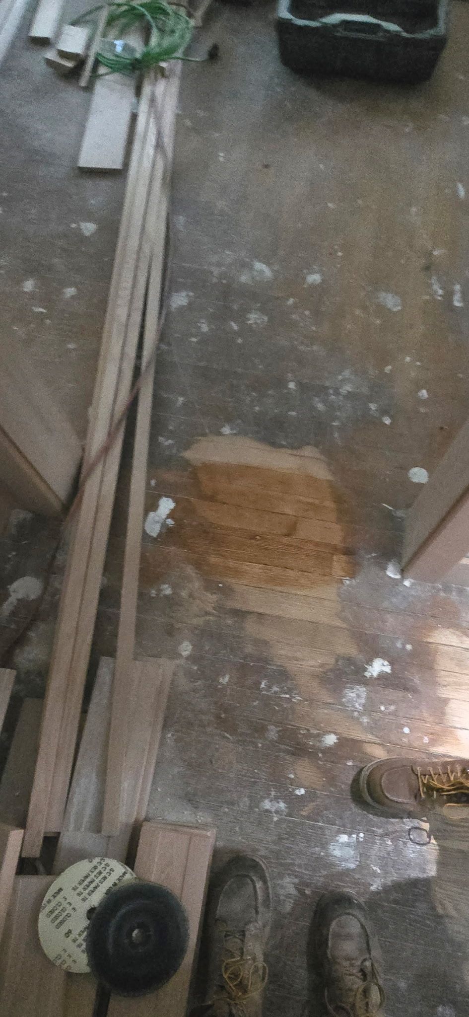 A construction site floor with debris, wooden boards, a circular saw blade, and a patch of exposed plywood subflooring.