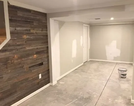 Basement room with concrete floor, wood accent wall, and painted walls, under construction.