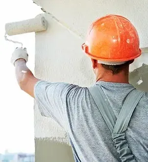 Construction worker in orange hard hat painting a wall with a roller.