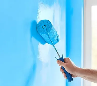 Hand painting a blue wall with a paint roller.