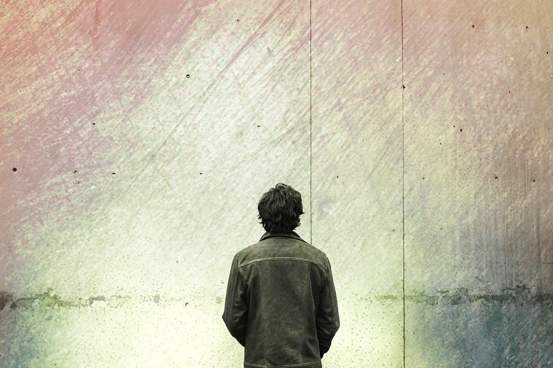 A man in a jacket is standing in front of a colorful wall.