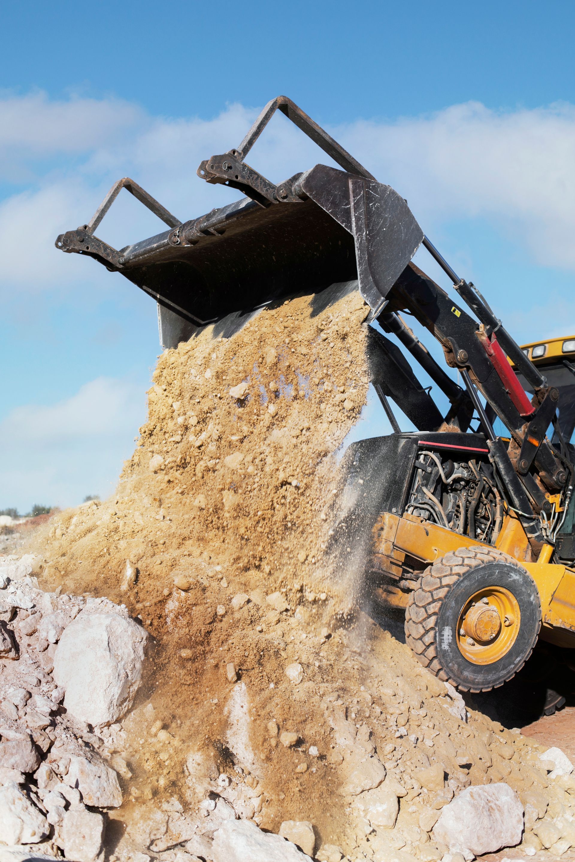 A bulldozer is dumping dirt into a pile of rocks.