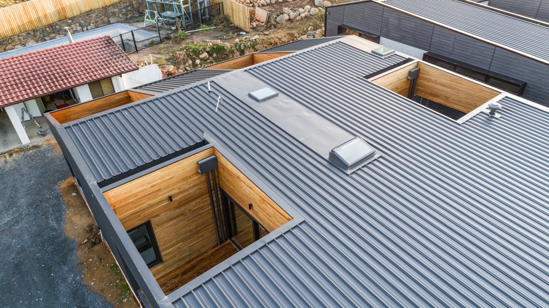 Overhead view of a modern gray metal roof with skylights and open wooden structural elements.