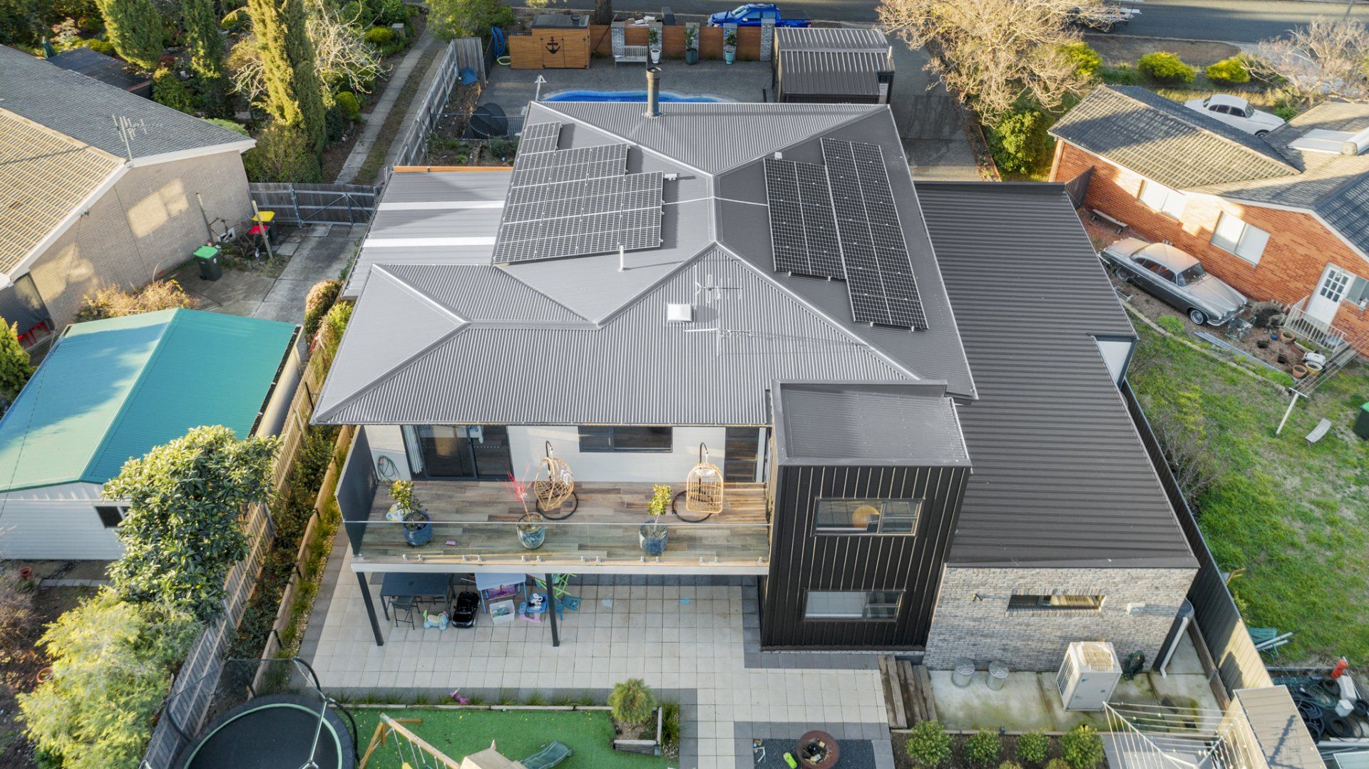 Aerial view of a modern house with solar panels, a deck, and a black accent wall.