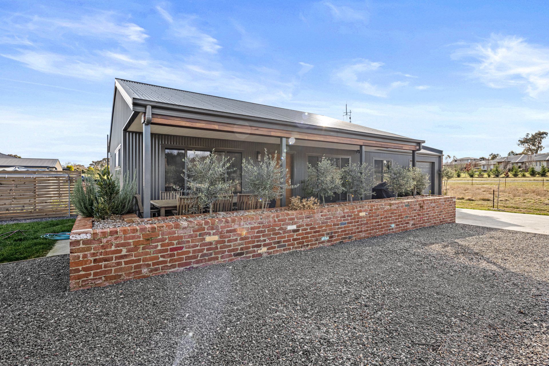 Modern gray house with brick wall and gravel driveway, under a blue sky.