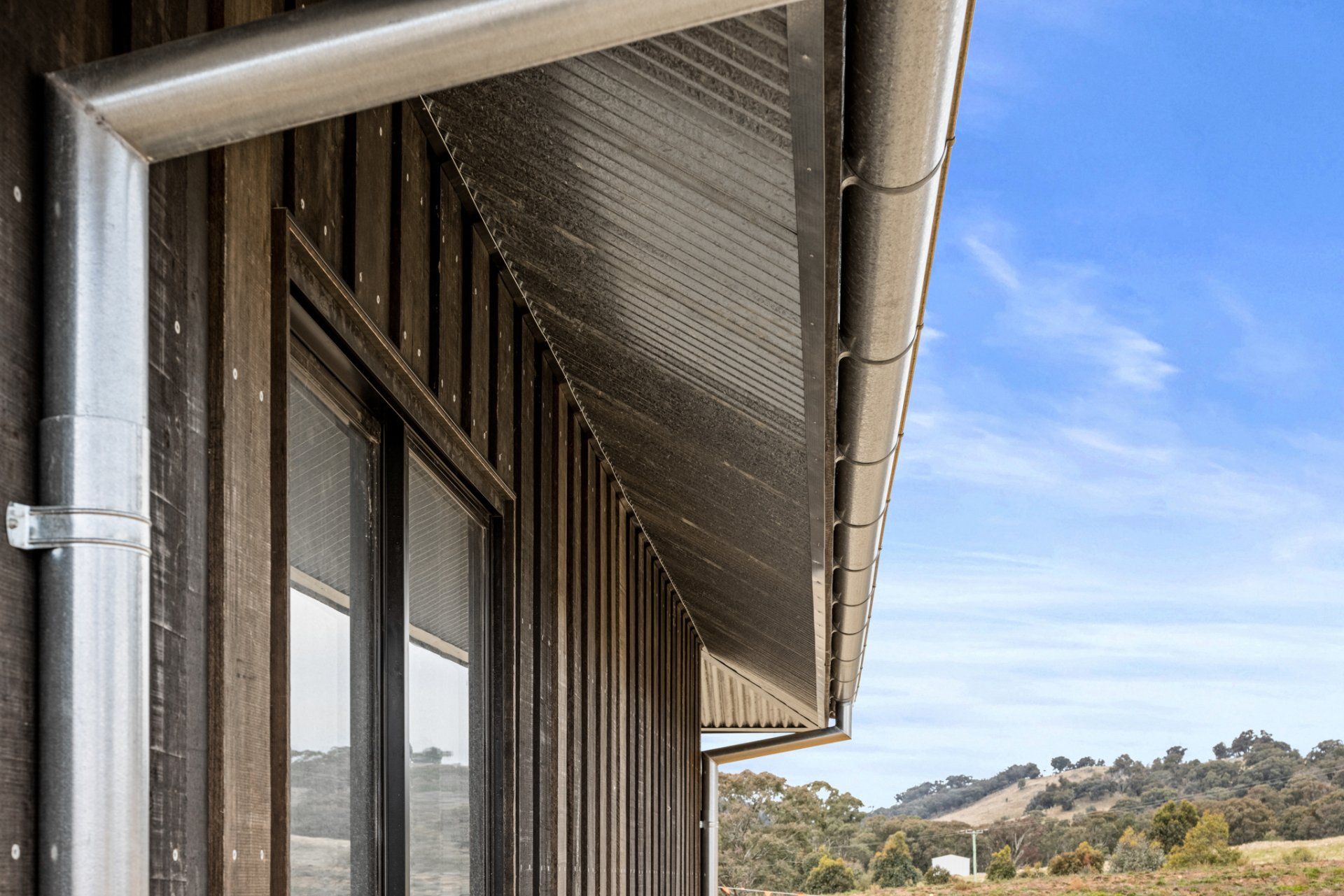 Exterior of a wooden building with metal gutters and downspouts against a blue sky.