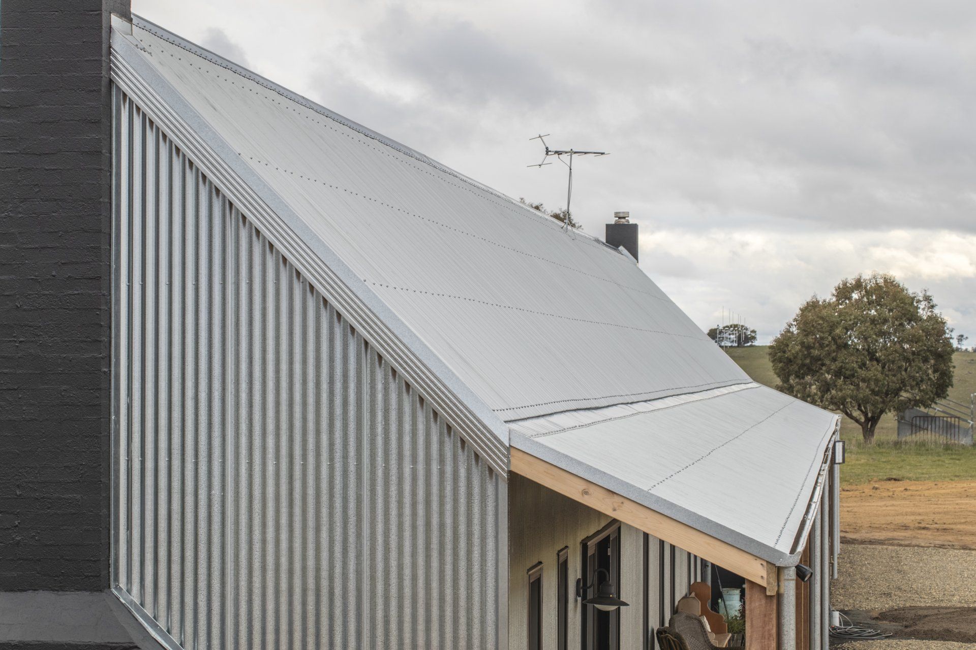 Angled metal roof on modern building with black chimney, overcast sky.