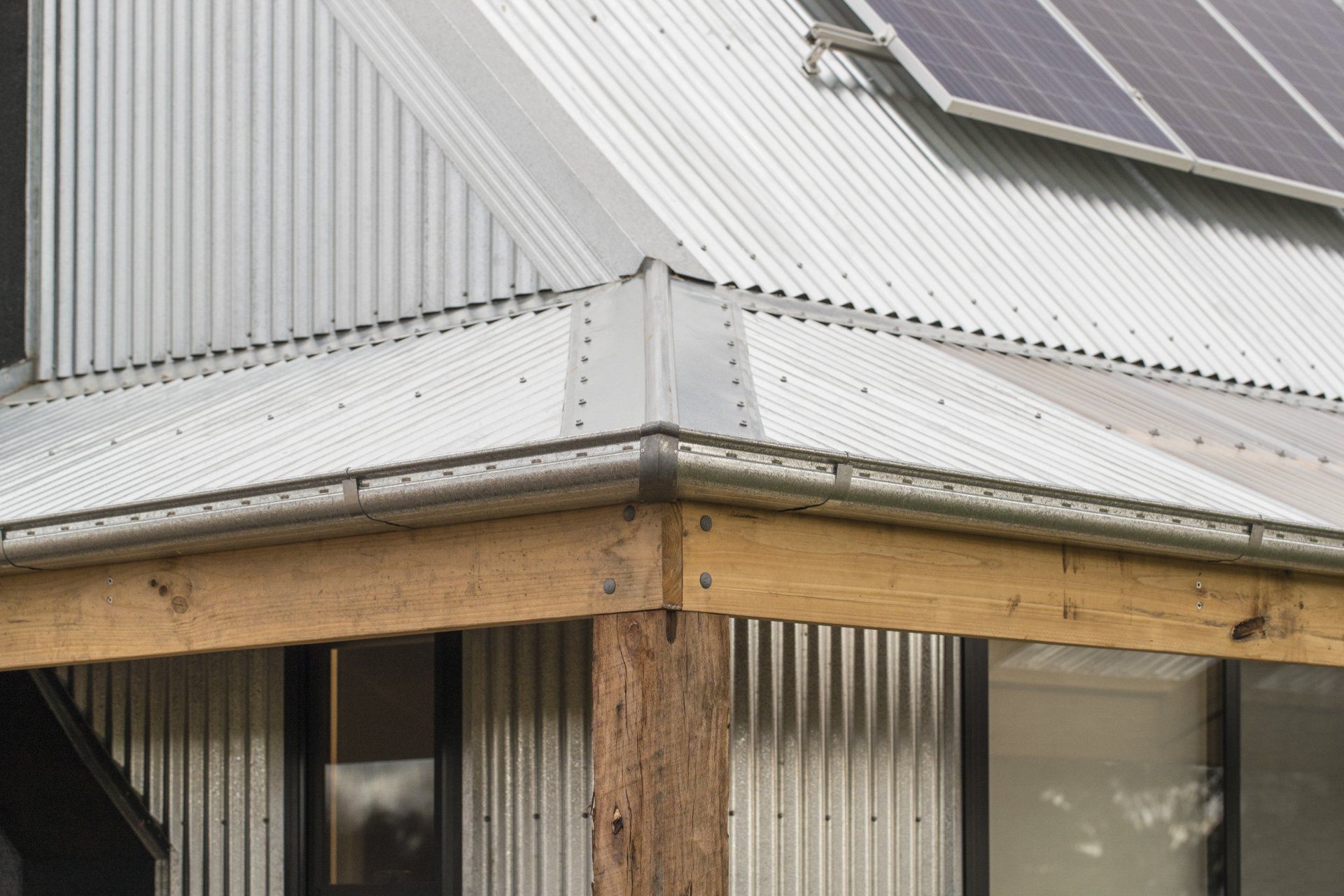Corrugated metal roof corner with wooden beam and solar panels.