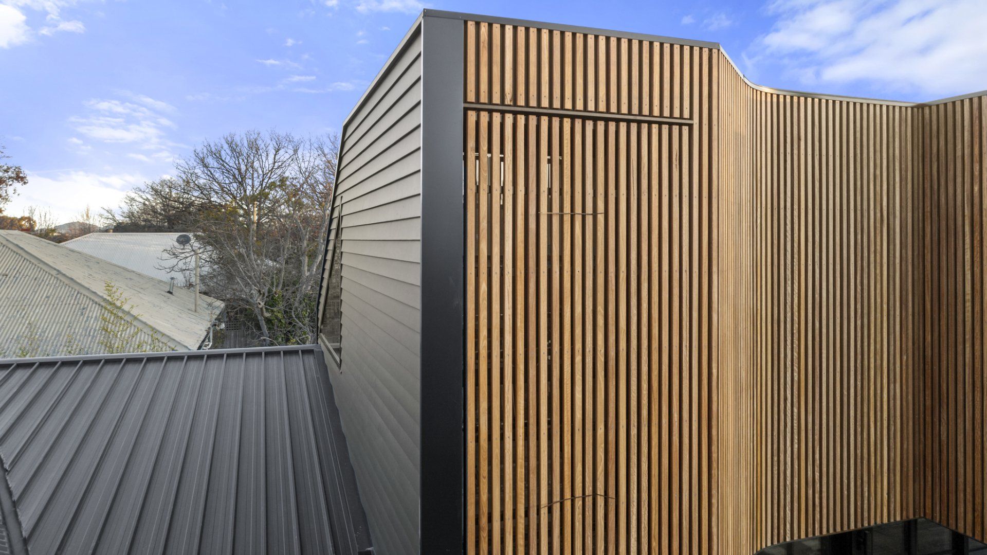 Modern building exterior with wood slat facade and gray siding against a blue sky.