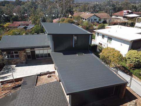 Aerial view of a modern house with a dark gray flat roof, and a carport in a suburban setting.