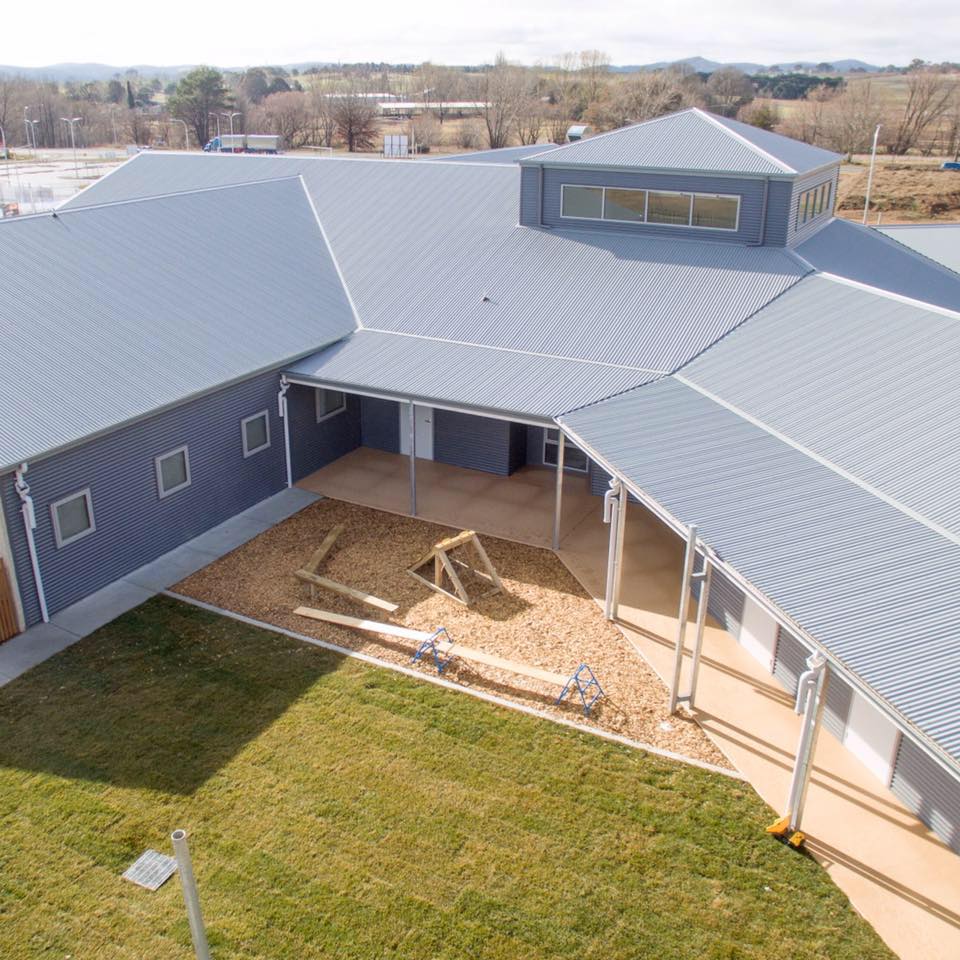 Blue building with a gray metal roof and an outdoor play area on a sunny day.