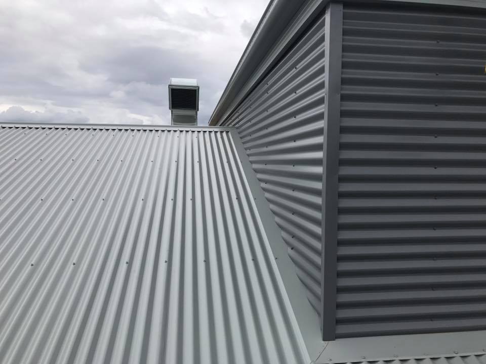 Gray corrugated metal roof and wall under a cloudy sky. A chimney sits on the roof.