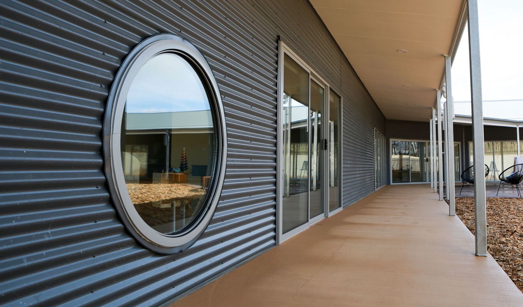 Exterior of a modern building with corrugated metal siding, a circular window, and a covered walkway.
