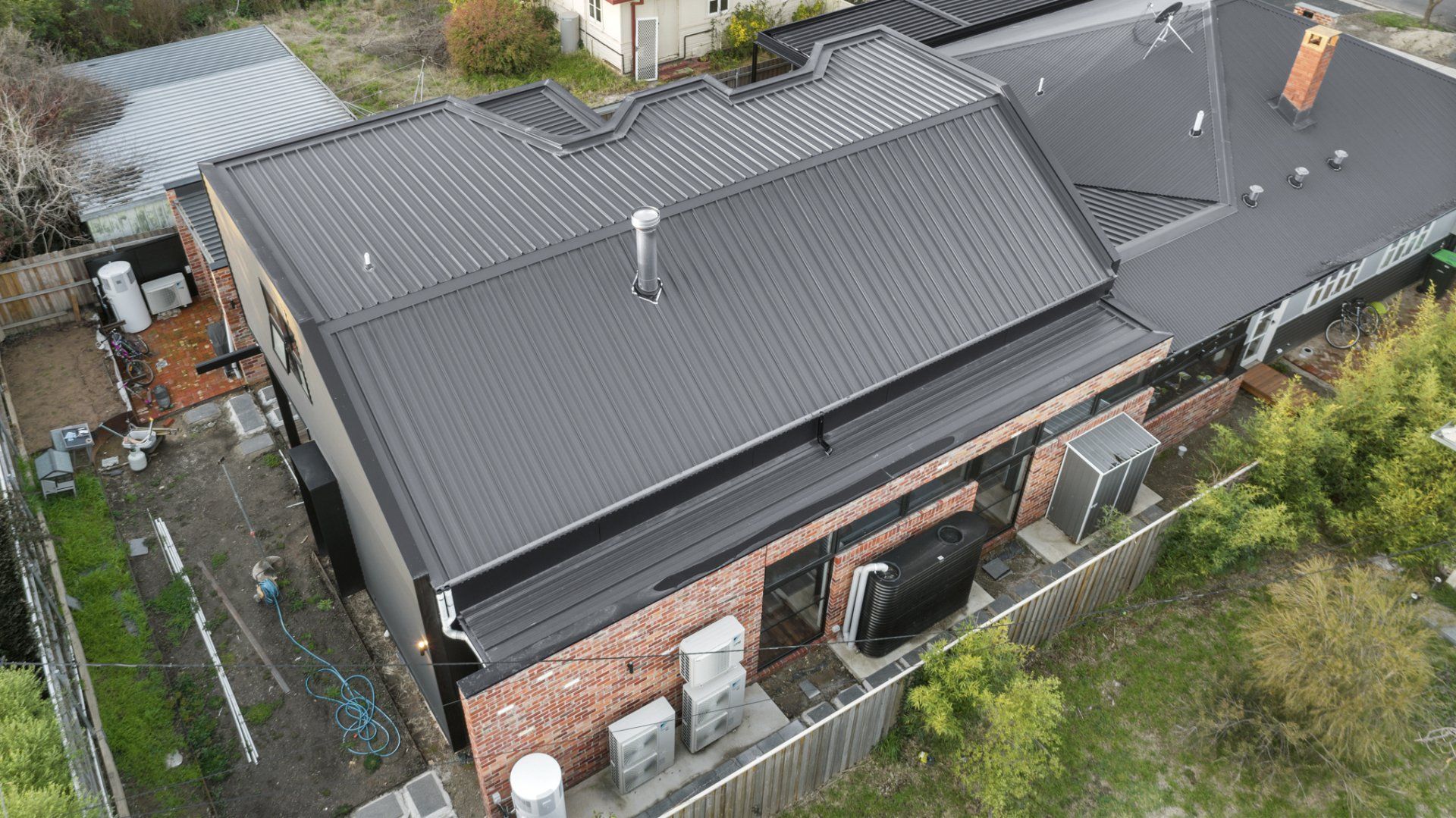 Black metal roof on a brick and black-trimmed building; aerial view.