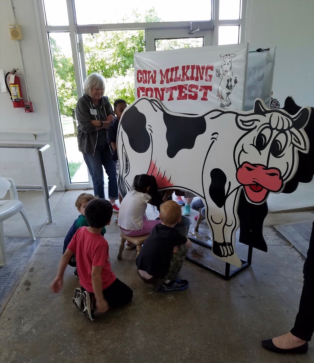 A group of children are pretend milking the comical milking cow