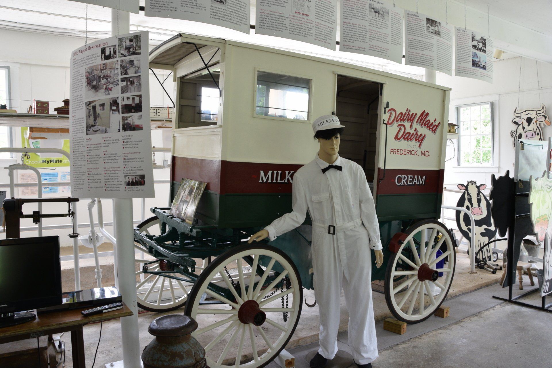 A milk man in uniform uniform is standing next to a horse drawn milk delivery carriage in the MOOseum.