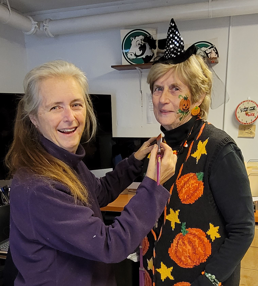 Woman paints face of another woman dressed for Halloween.
