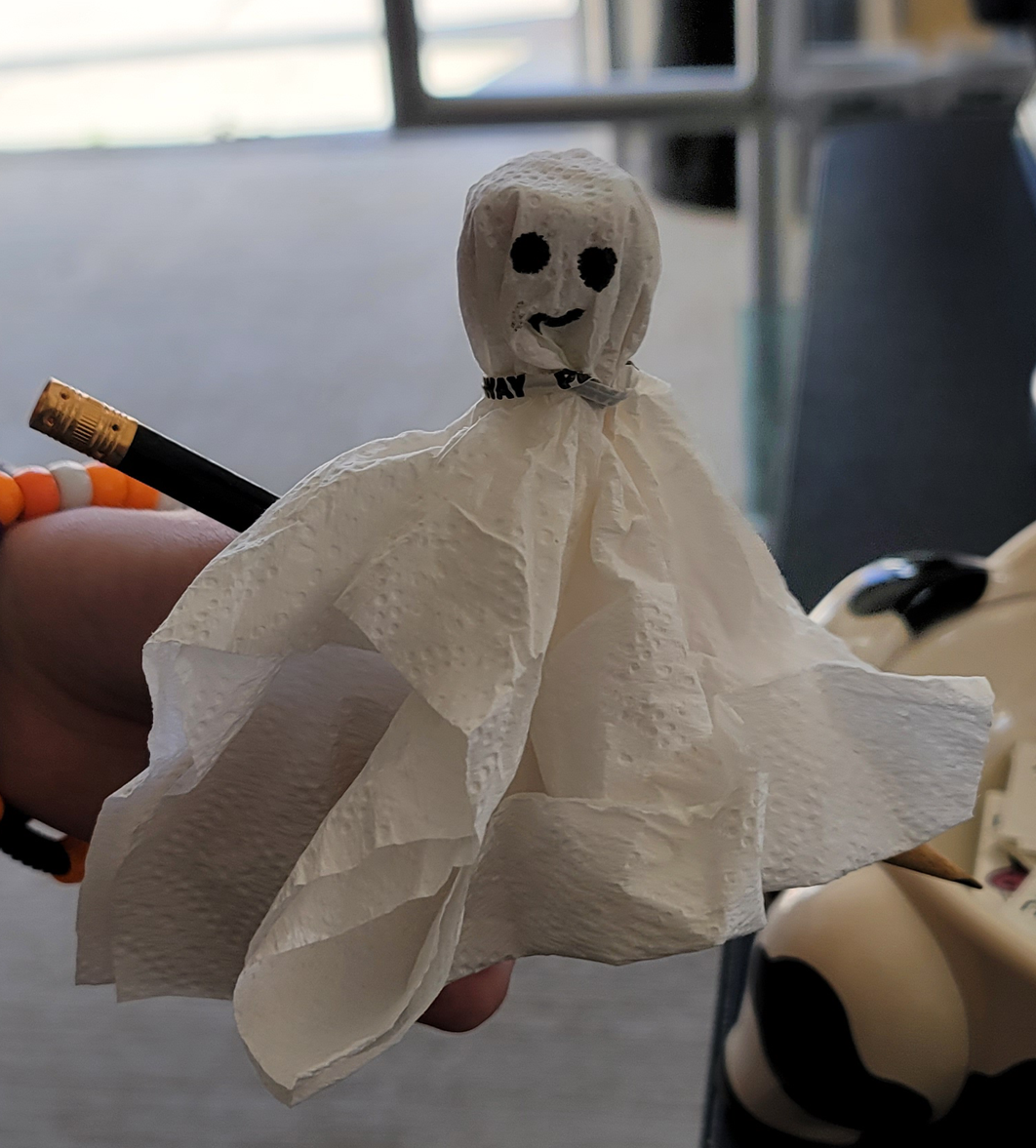 A small, white tissue paper ghost with drawn-on eyes and a smile, held by a person.