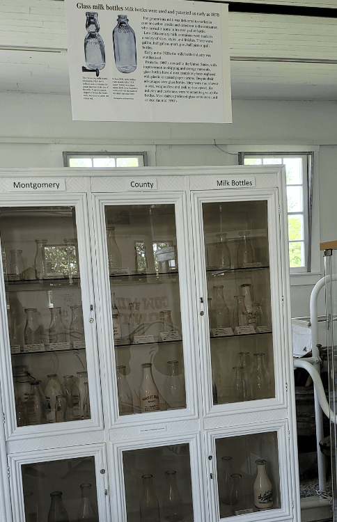 A white cabinet with glass doors filled with milk bottles