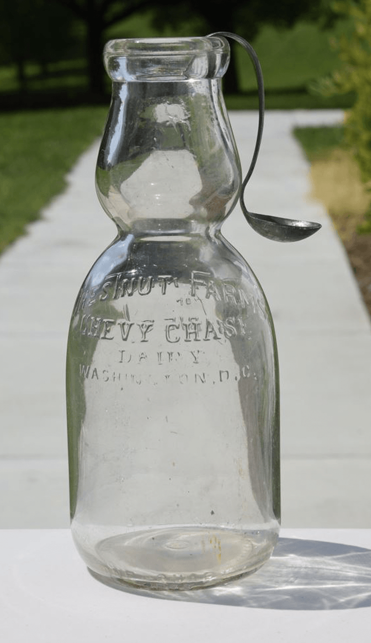 A milk bottle with a handle is sitting on a sidewalk.