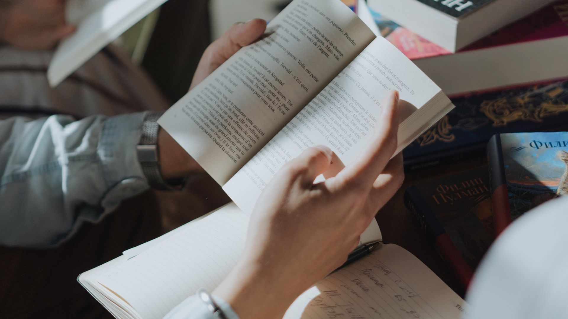 A person is reading a book in front of a stack of books.