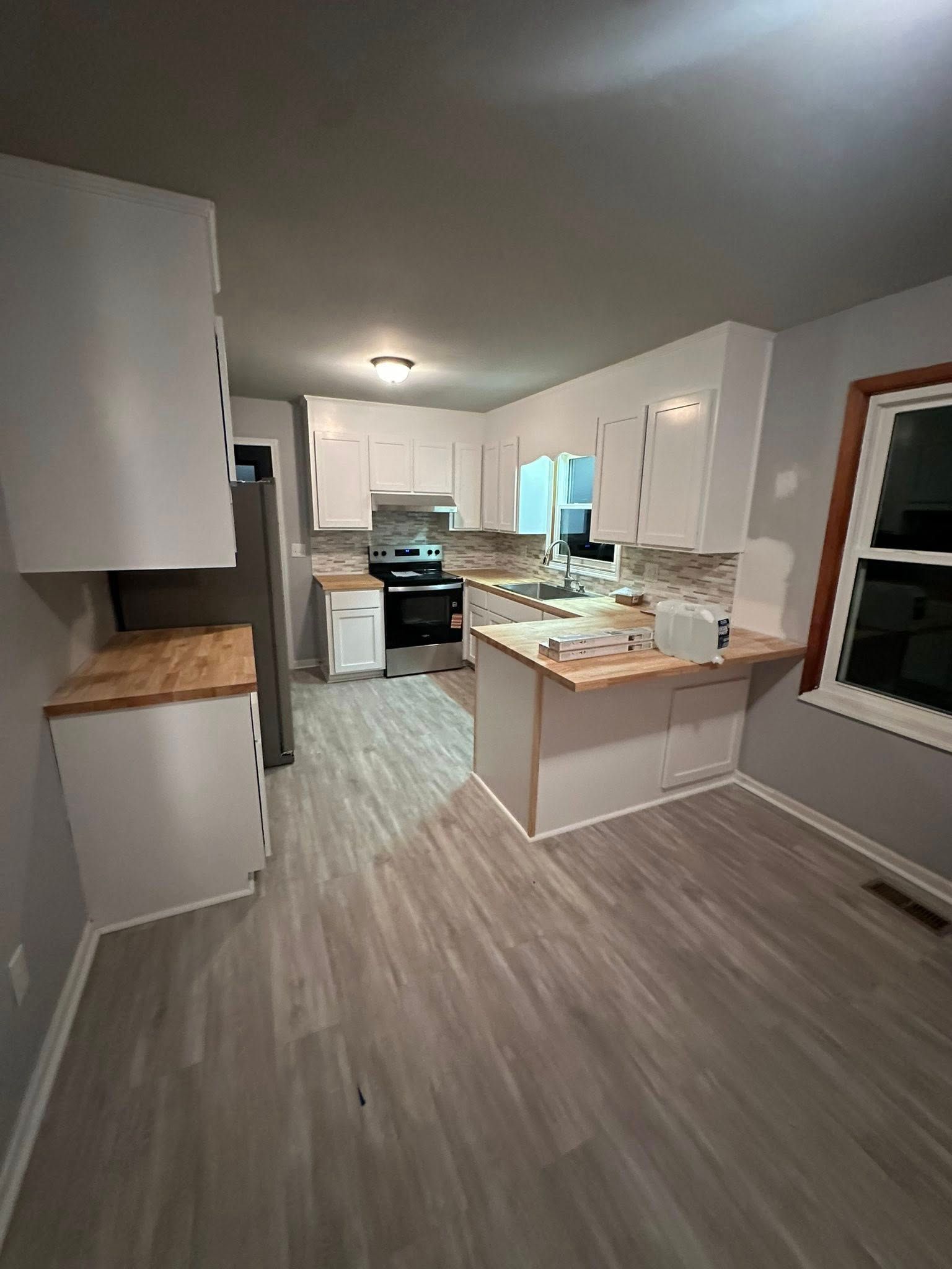 Bright kitchen with white cabinets, wood countertops, gray flooring, and stainless steel stove.