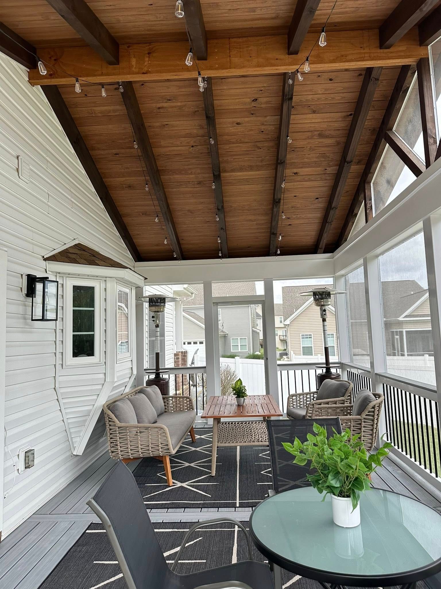 Covered porch with wicker seating, a glass-top table, and a dark wood vaulted ceiling.