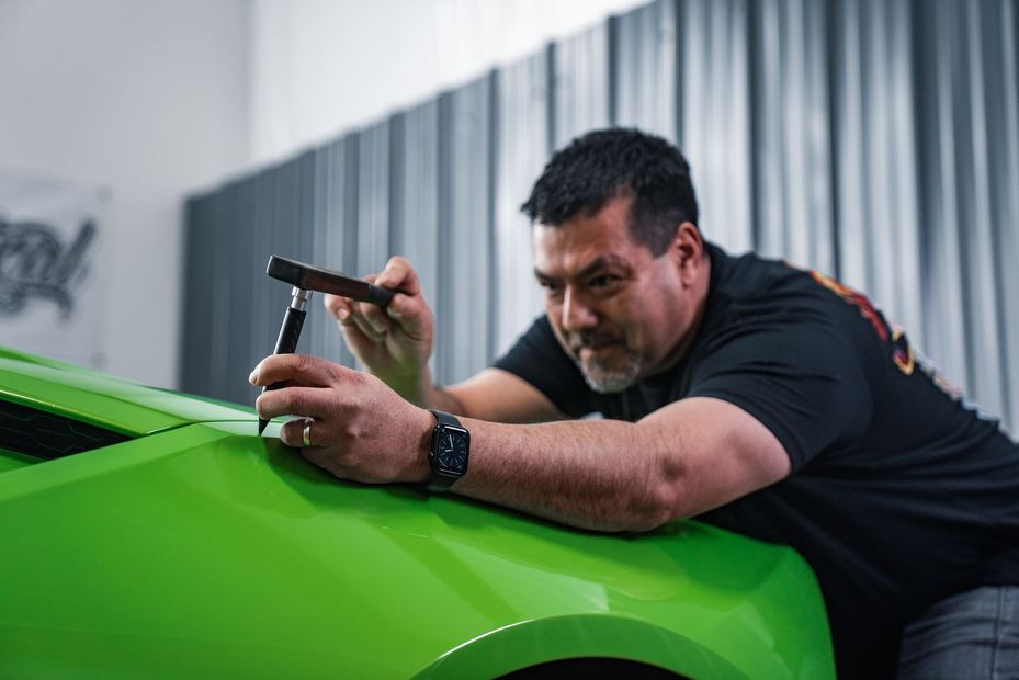 Owner working on green car with tools. focused expression. In a shop