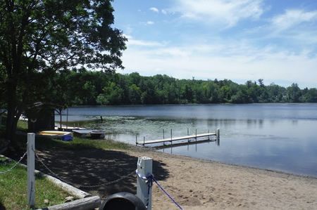 A lake with a dock and boats on the shore on a sunny day – Oxford, MI - Camp Oakland