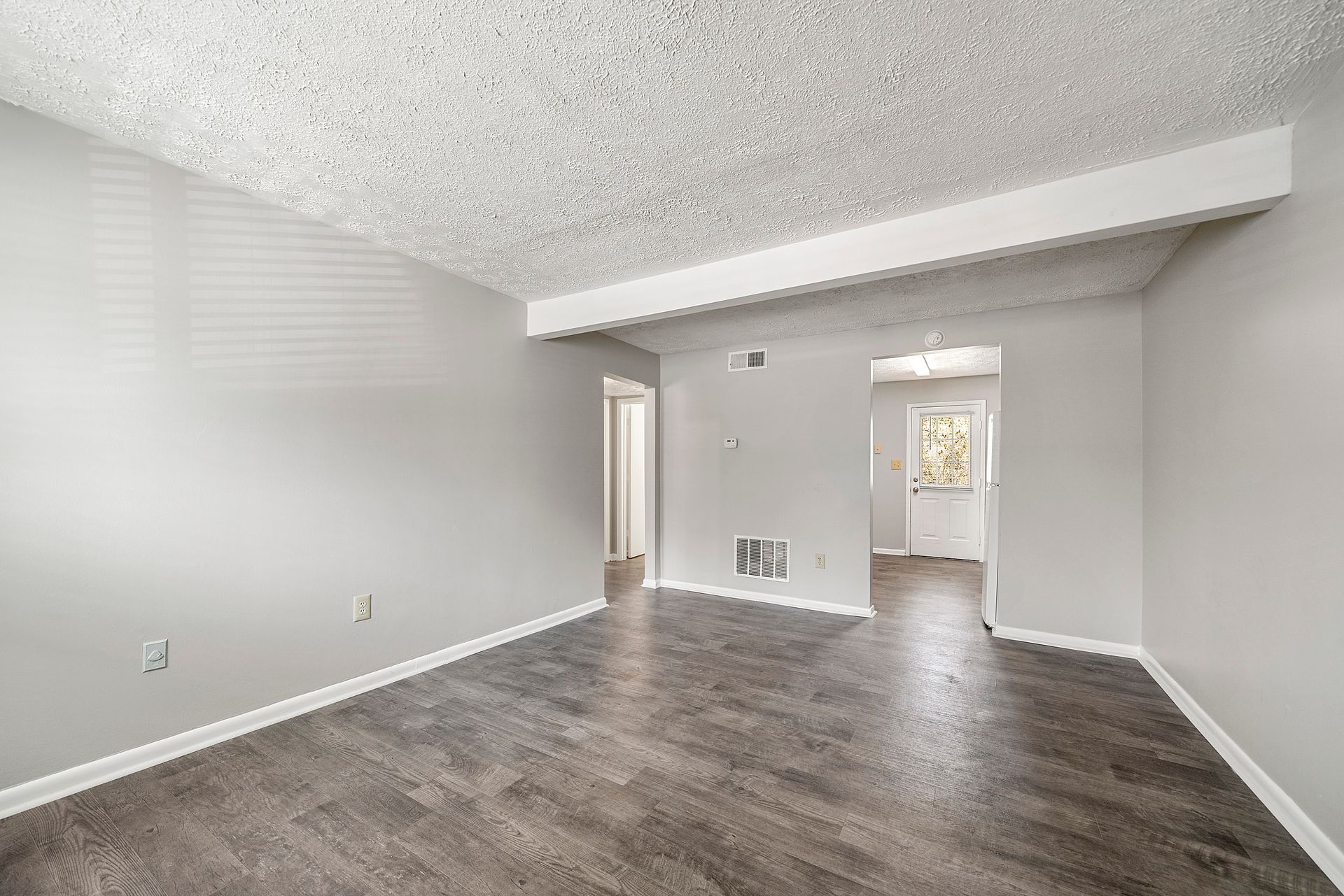 Empty gray living room with dark wood floors, white trim, and an open doorway to another room