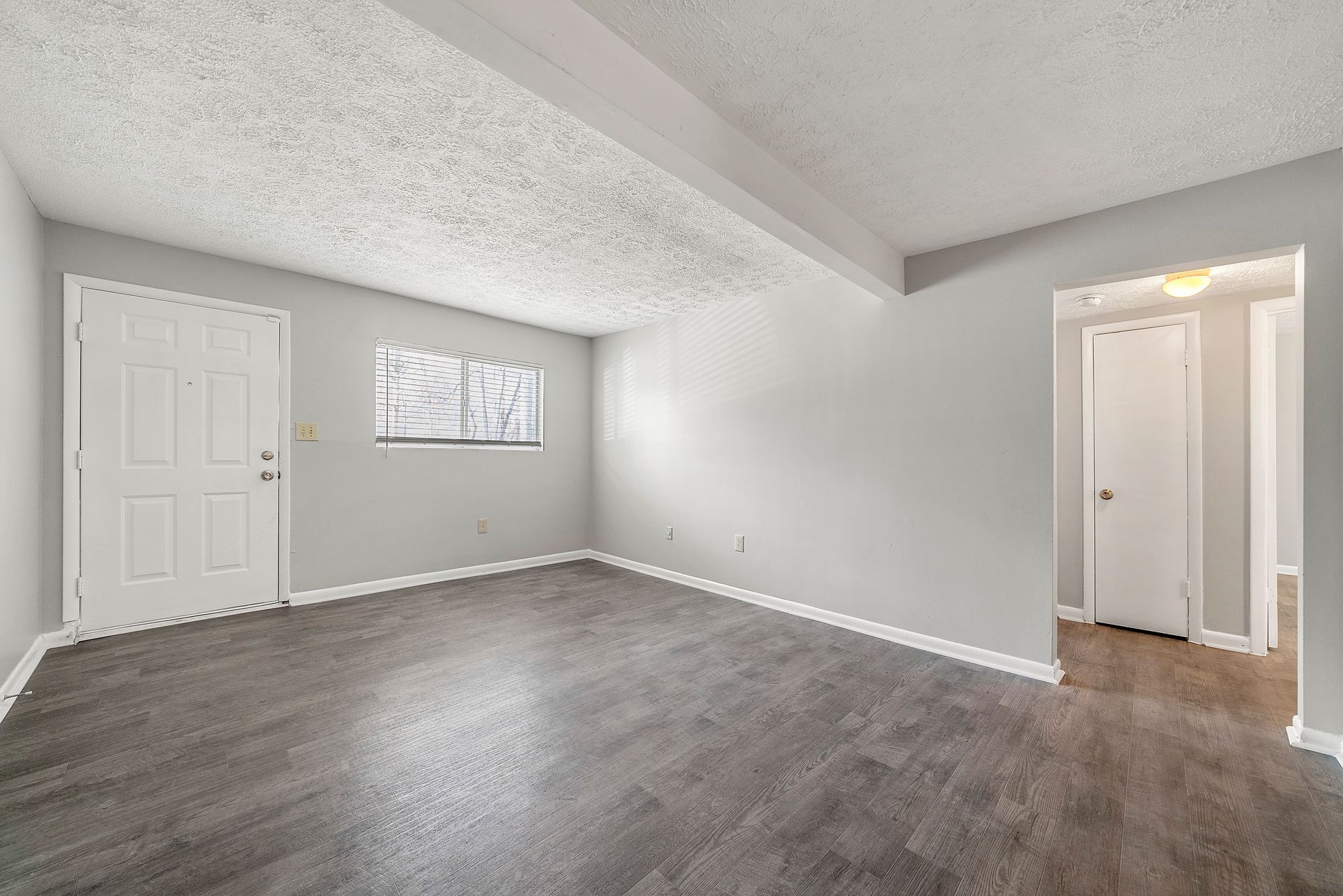 Empty gray bedroom with carpet, white trim, a closet, window, and open doorway to hall