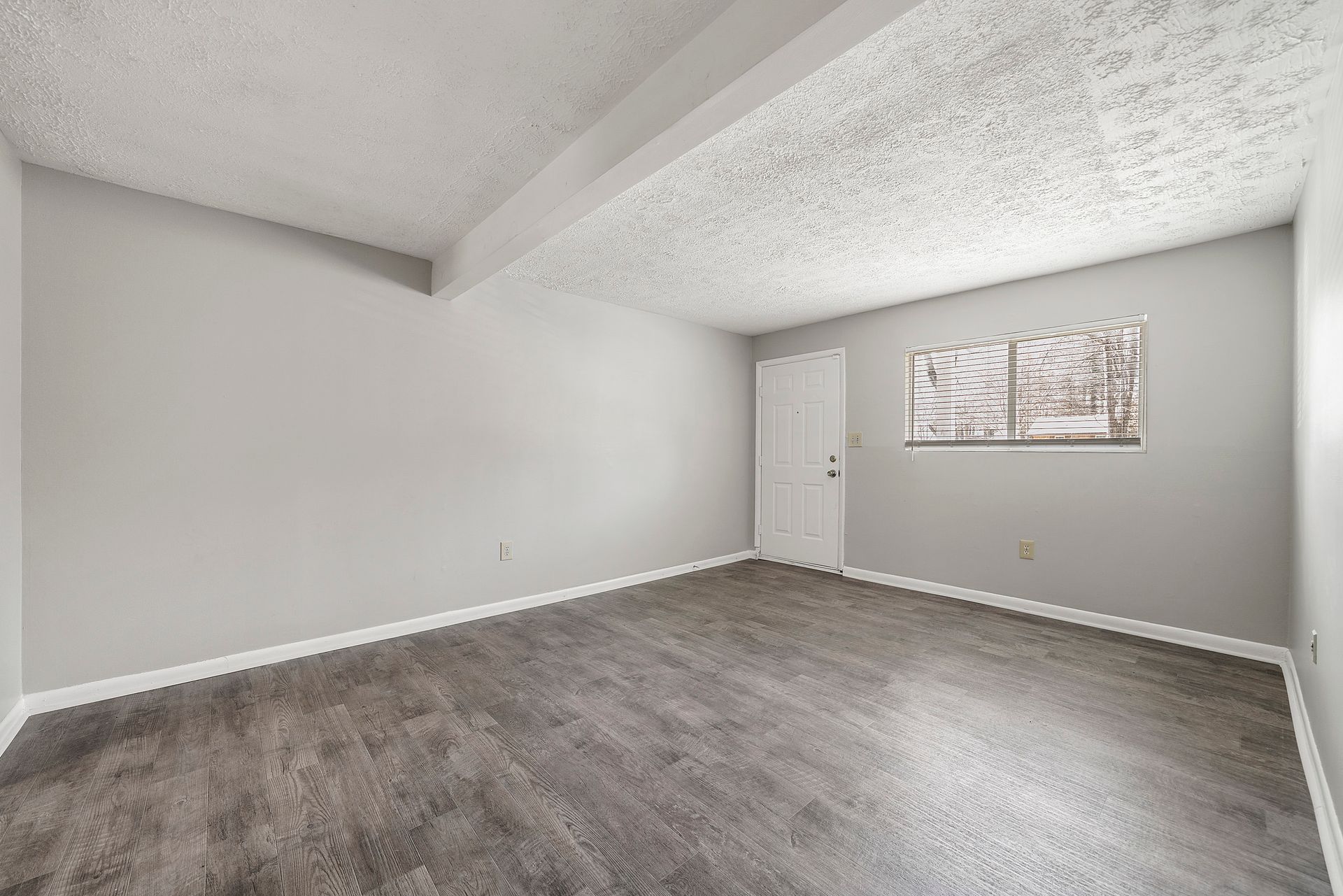 Empty gray bedroom with textured ceiling, white door, and wall art.