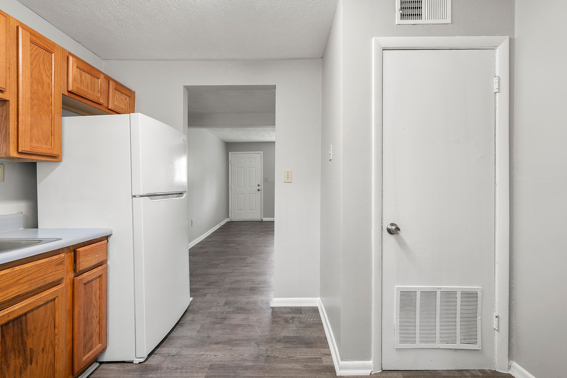 Small kitchen with wooden cabinets, white refrigerator, and a hallway leading to a door