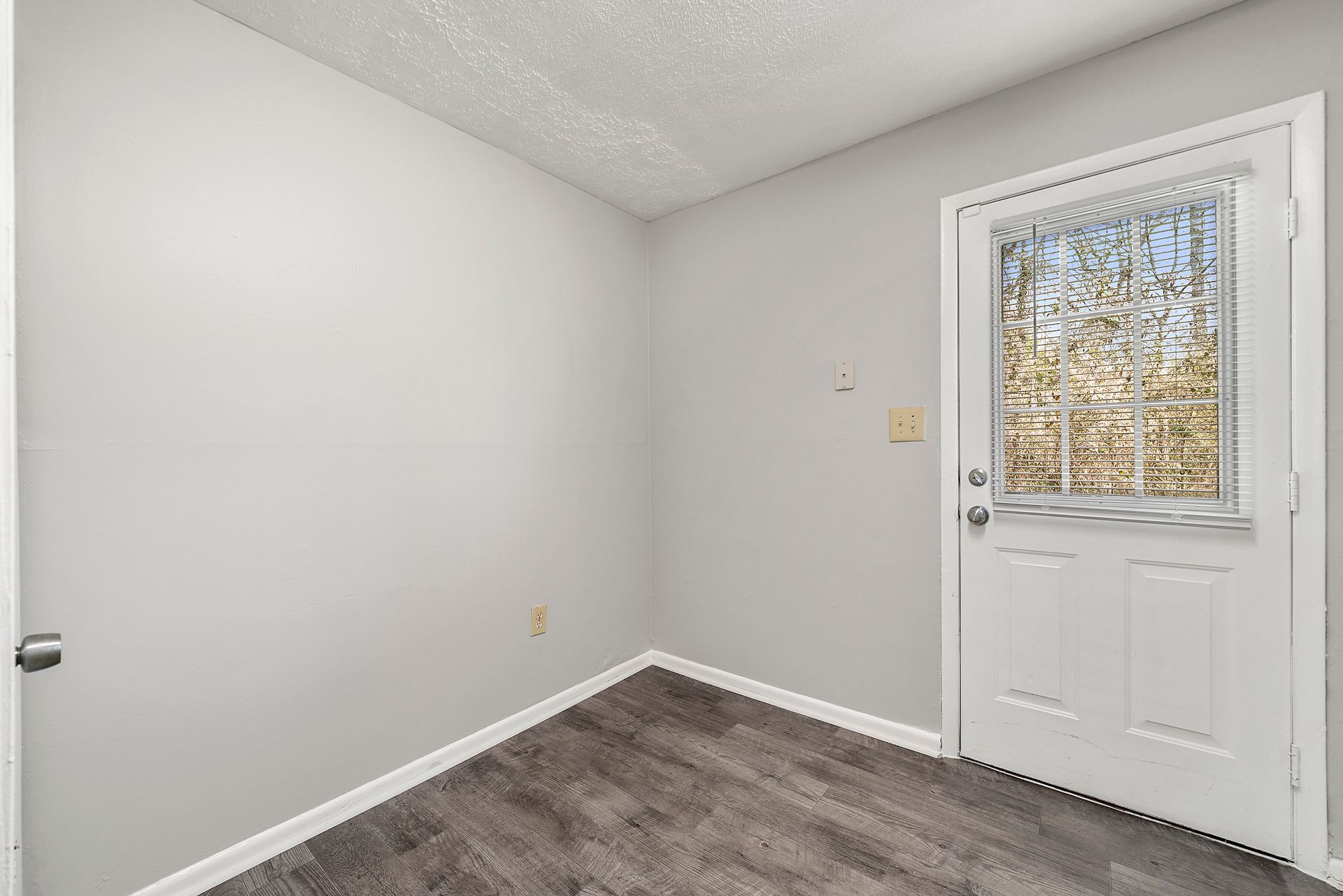 Small empty room with gray walls, carpet, and a white door with a window.