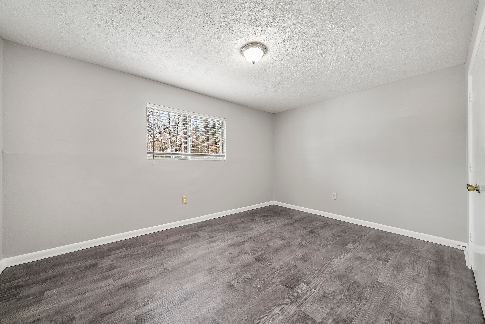Empty gray bedroom with carpet, white walls, a small window, and a ceiling light.