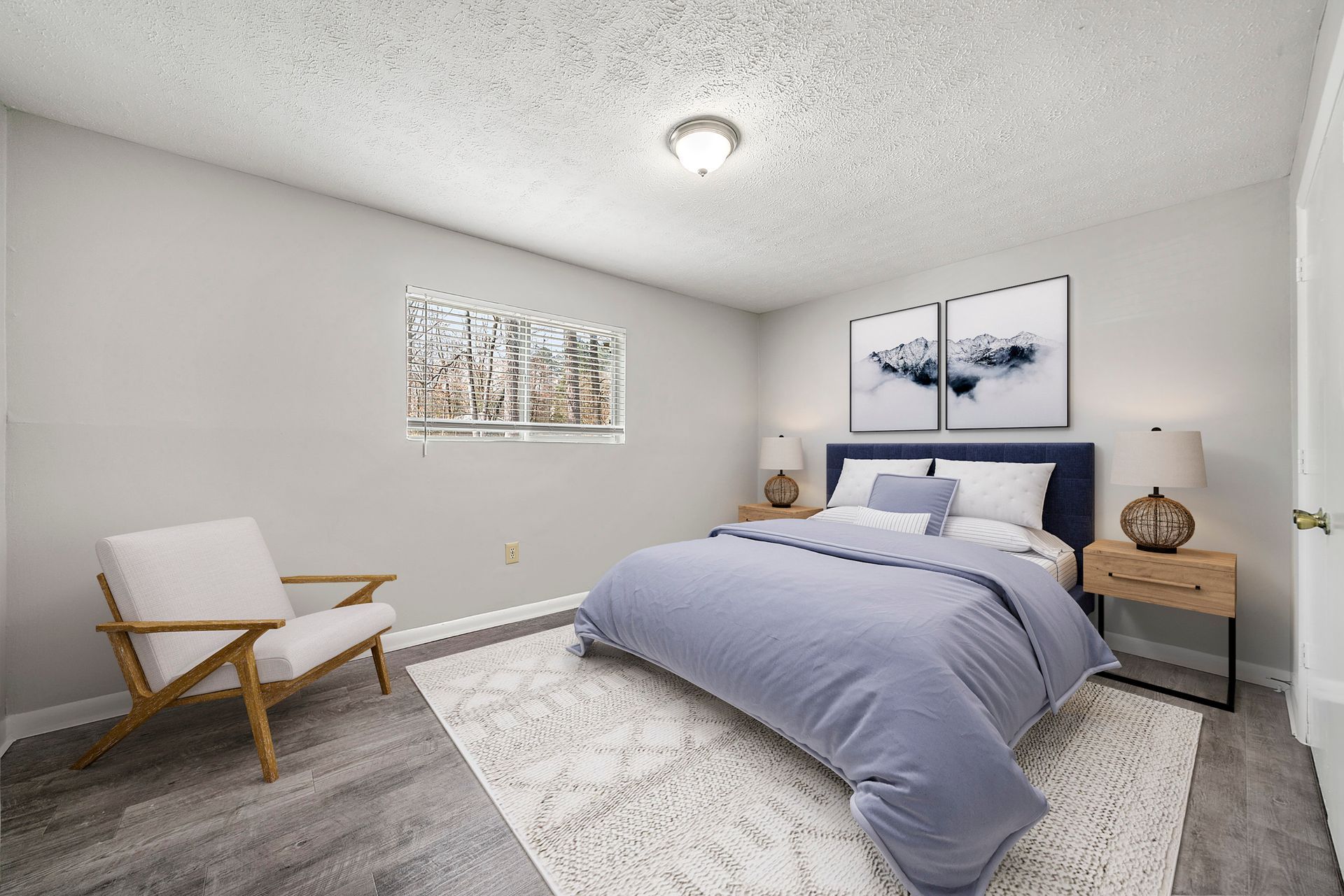 Bright bedroom with blue bed, white chair, nightstands, and wall art on a light gray carpet.