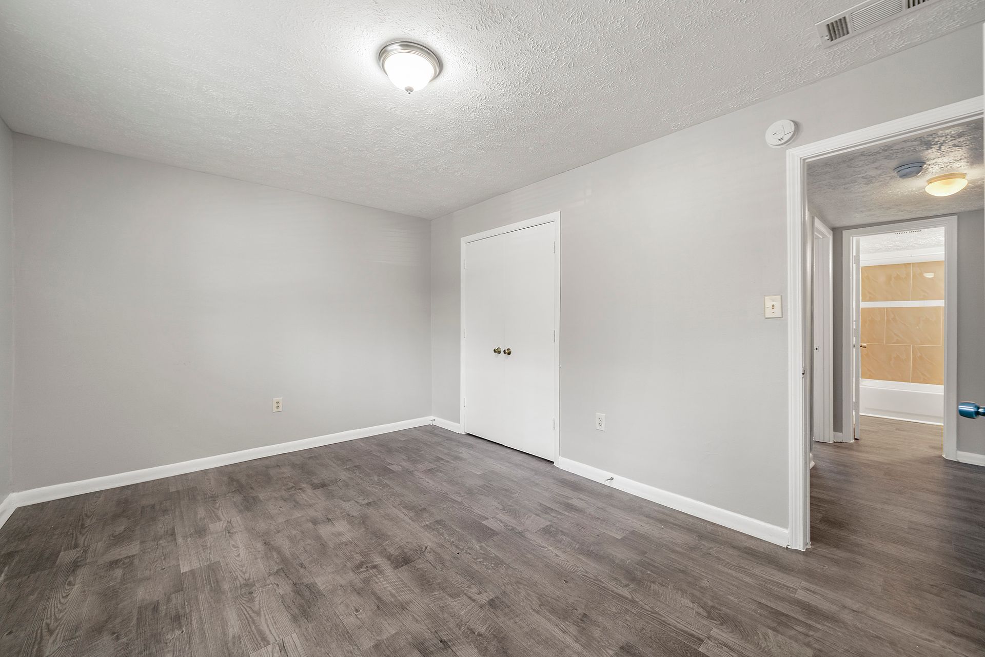 Empty gray bedroom with white closet doors and dark wood-style flooring