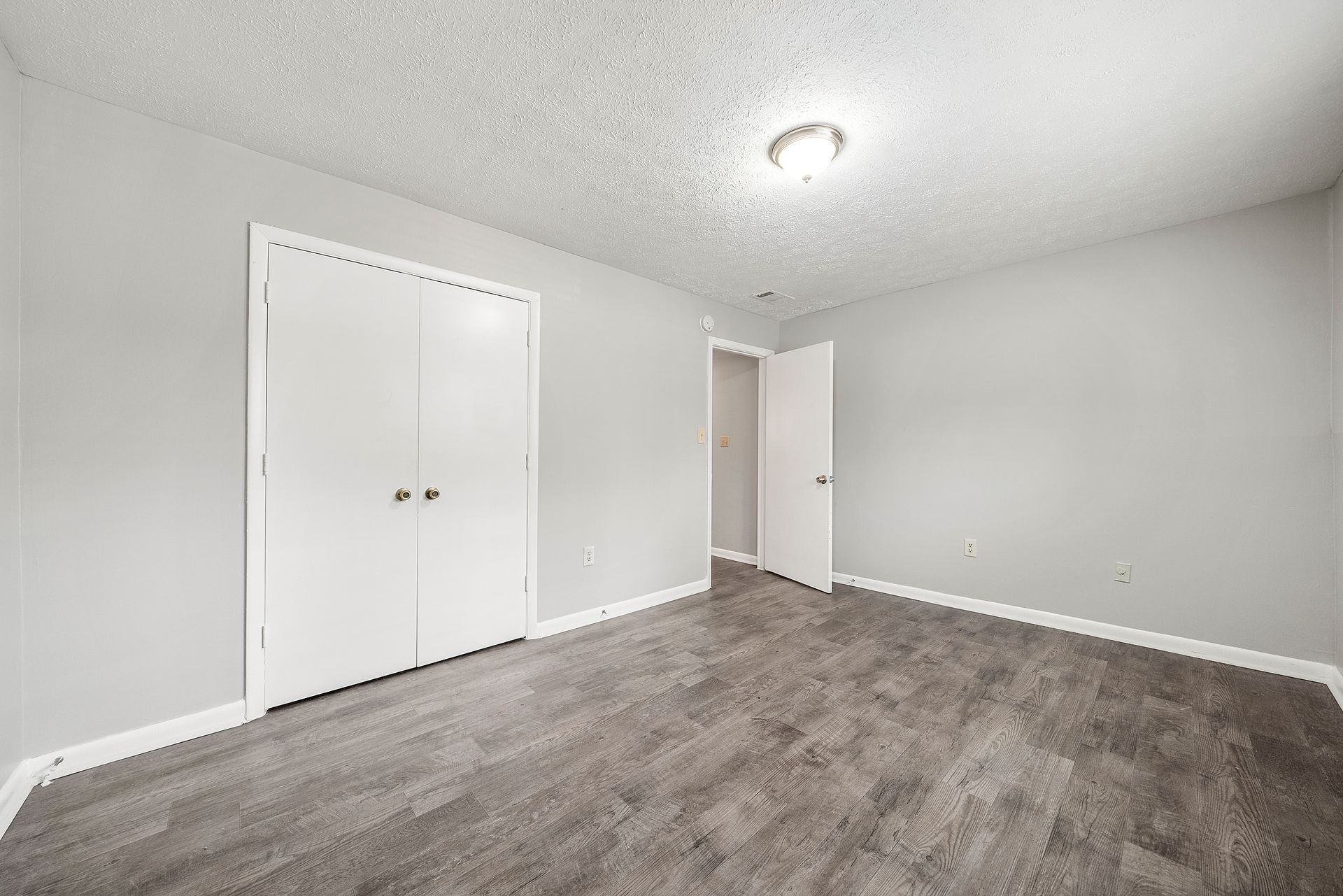 Empty gray bedroom with carpet, closet doors, and a ceiling light