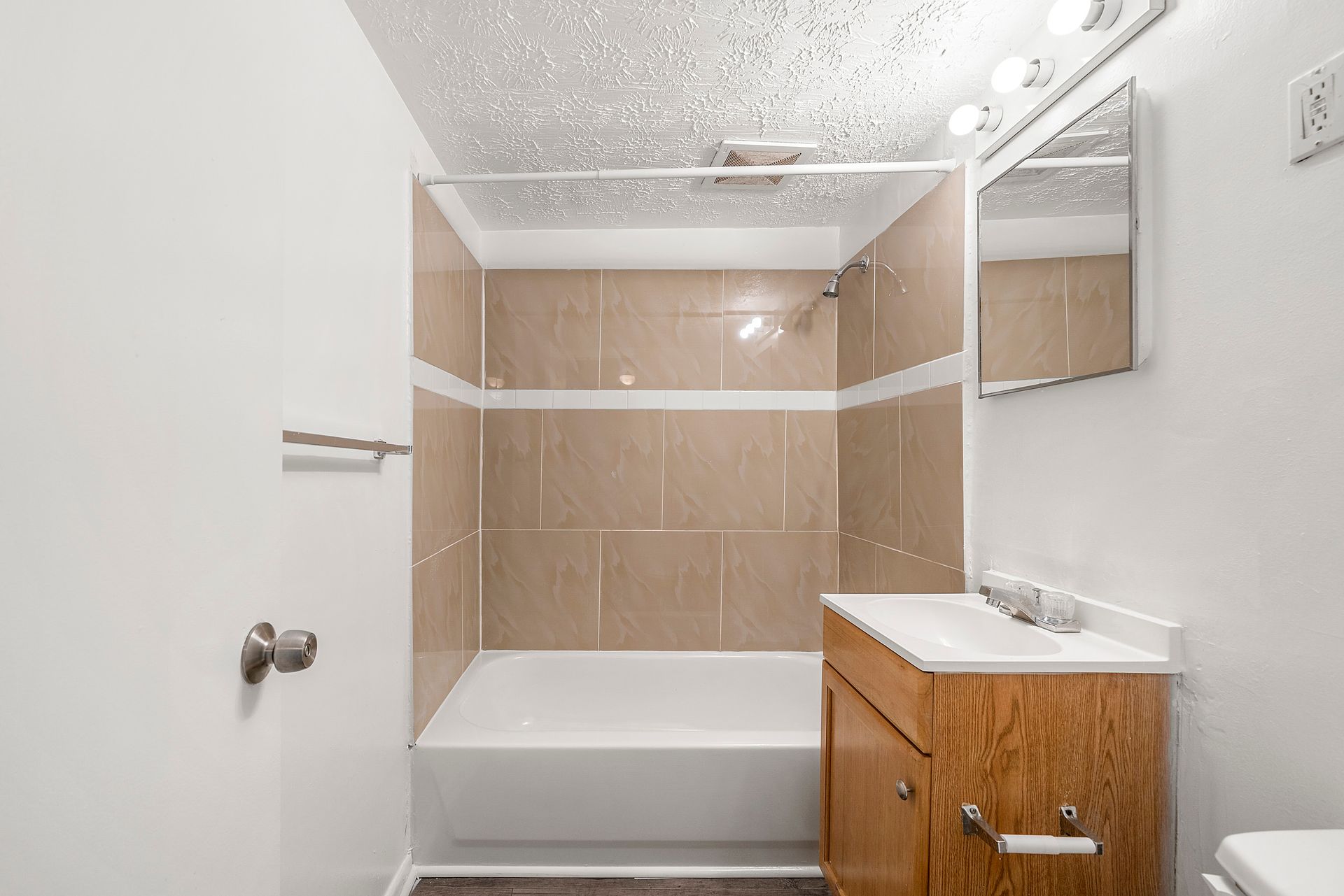Bathroom with white tub, beige tile walls, wood vanity, and speckled ceiling panel.