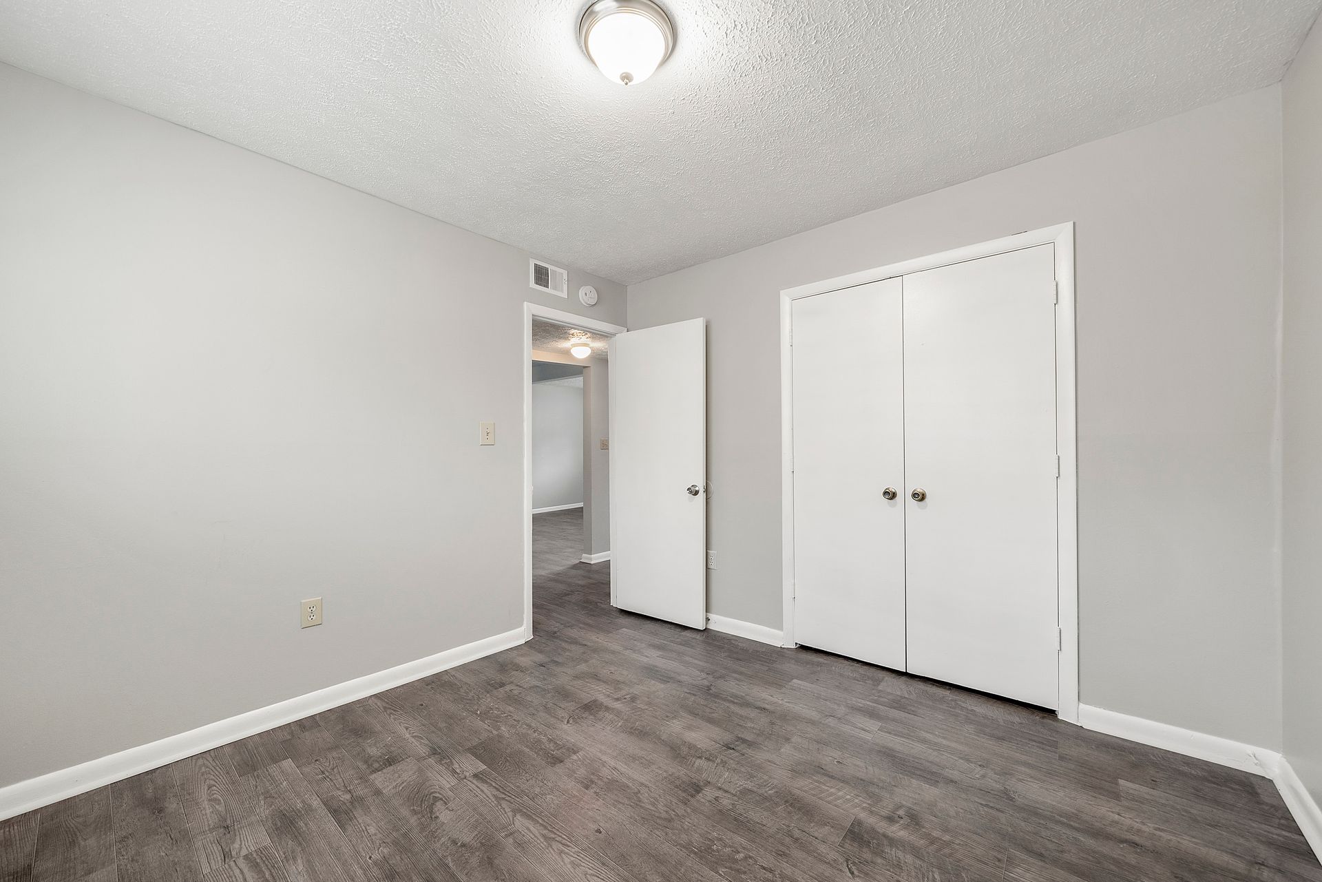 Empty gray bedroom with white closet doors, open doorway, and wood-look flooring