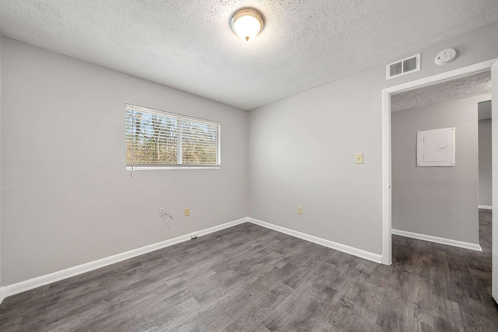 Empty gray bedroom with white trim, carpeted floor, small window, and open doorway to hallway