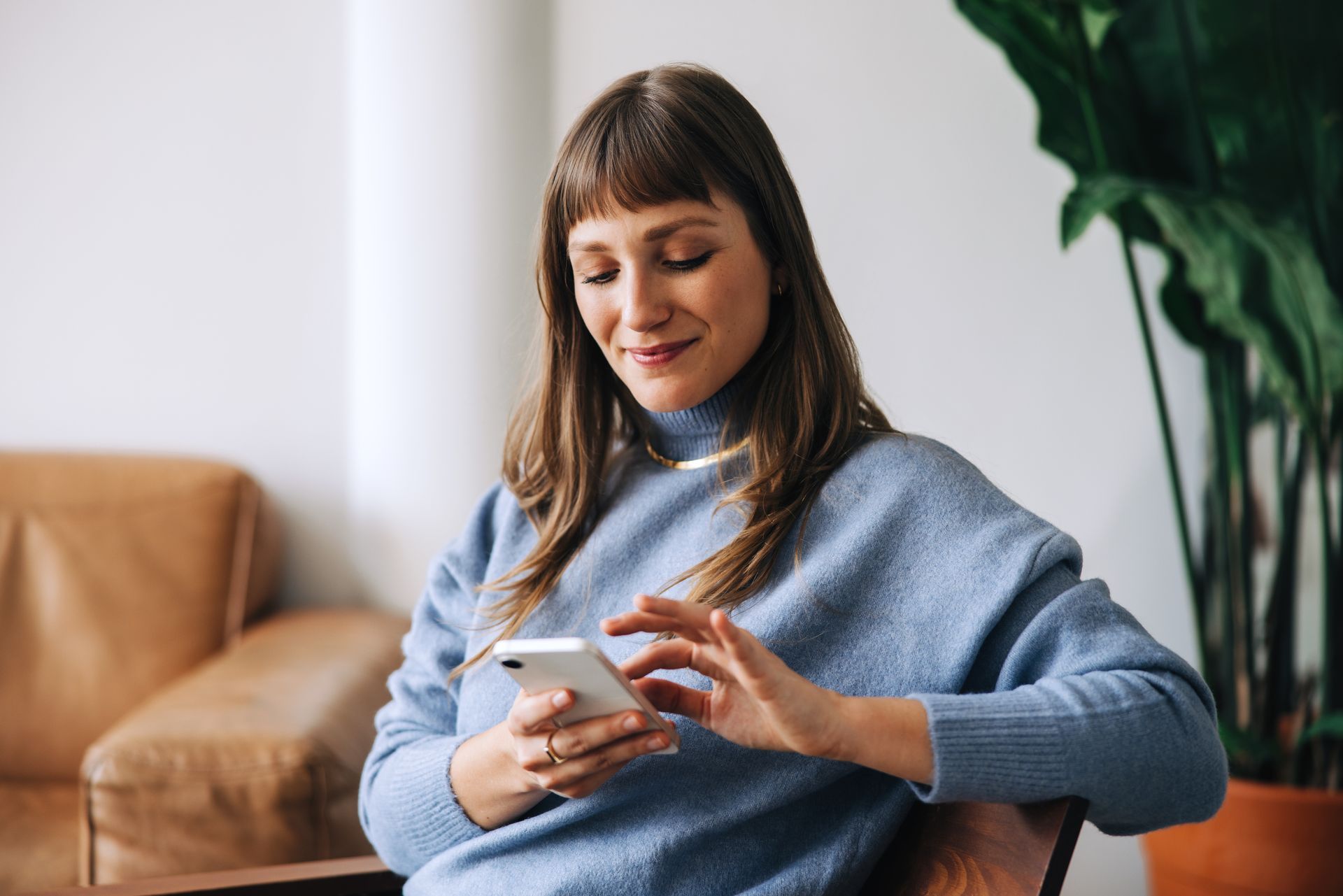 Person in a blue sweater using a smartphone while sitting on a couch indoors.