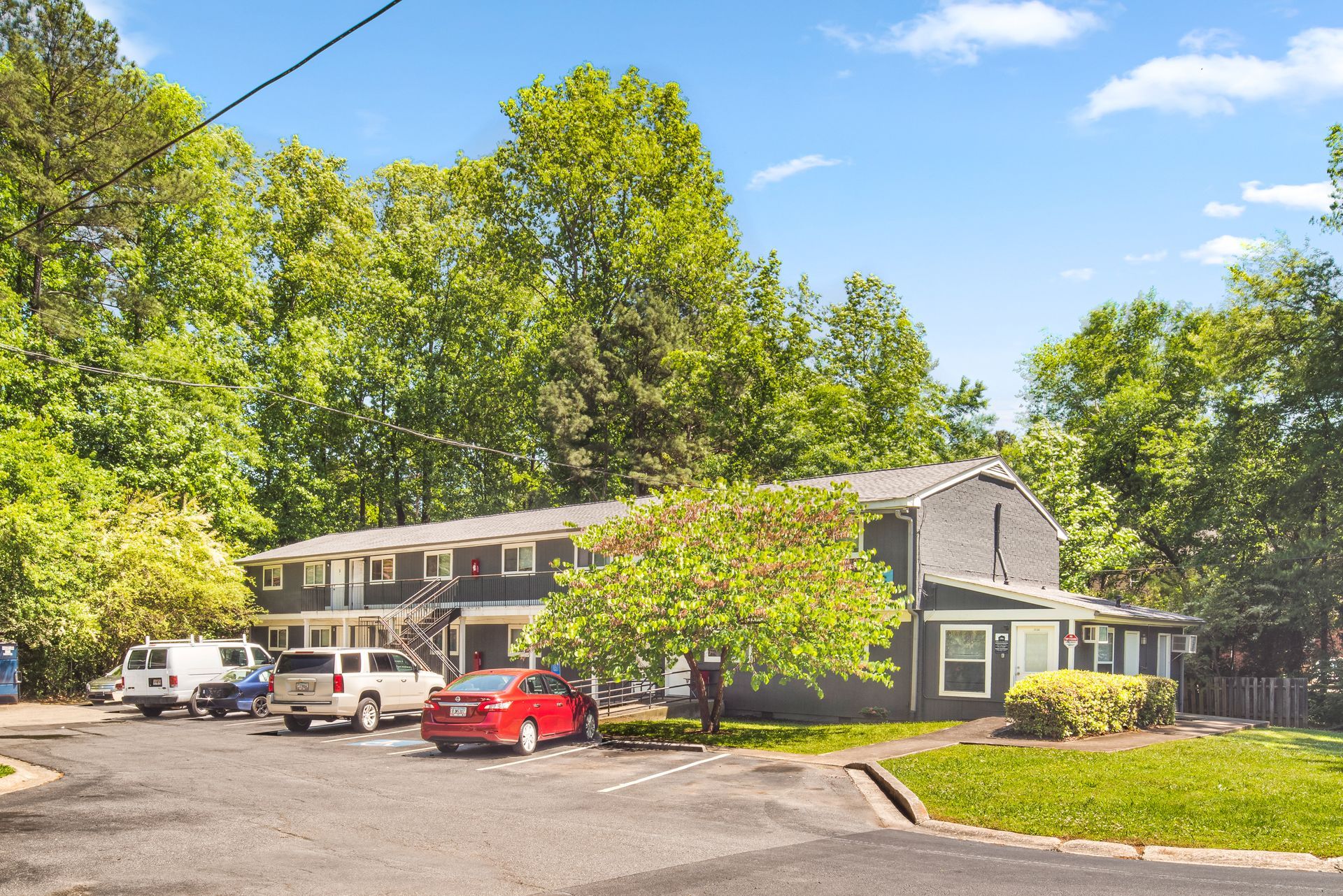 Apartment building with parked cars under green trees on a sunny day