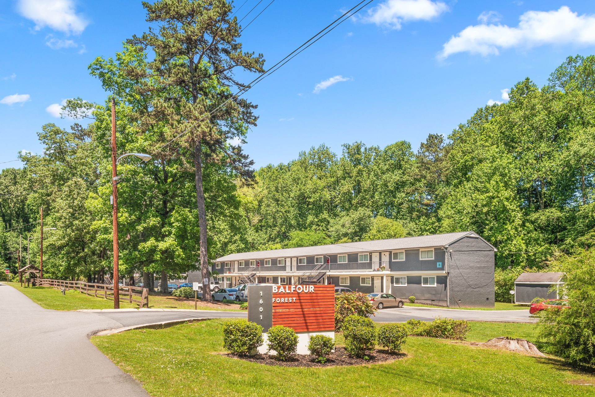 Mobile home park entrance with a red sign, curving road, and trees under a blue sky