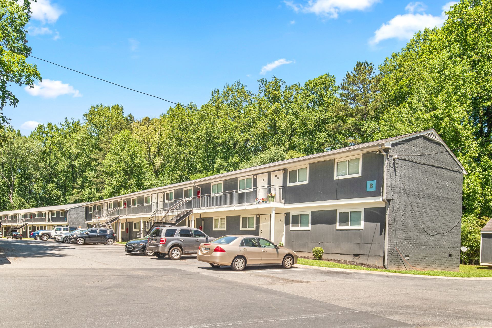 Row of gray apartment buildings with parked cars under a bright blue sky