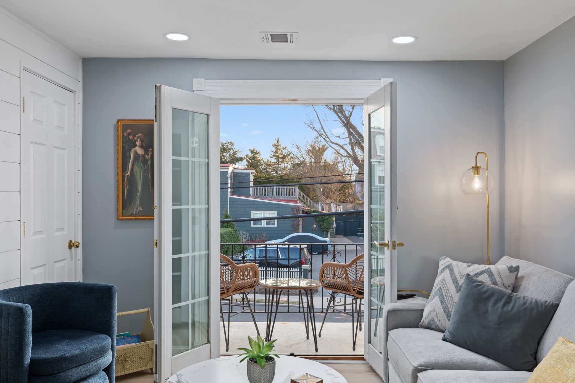 A living room with a couch , chair , table and french doors leading to a balcony.