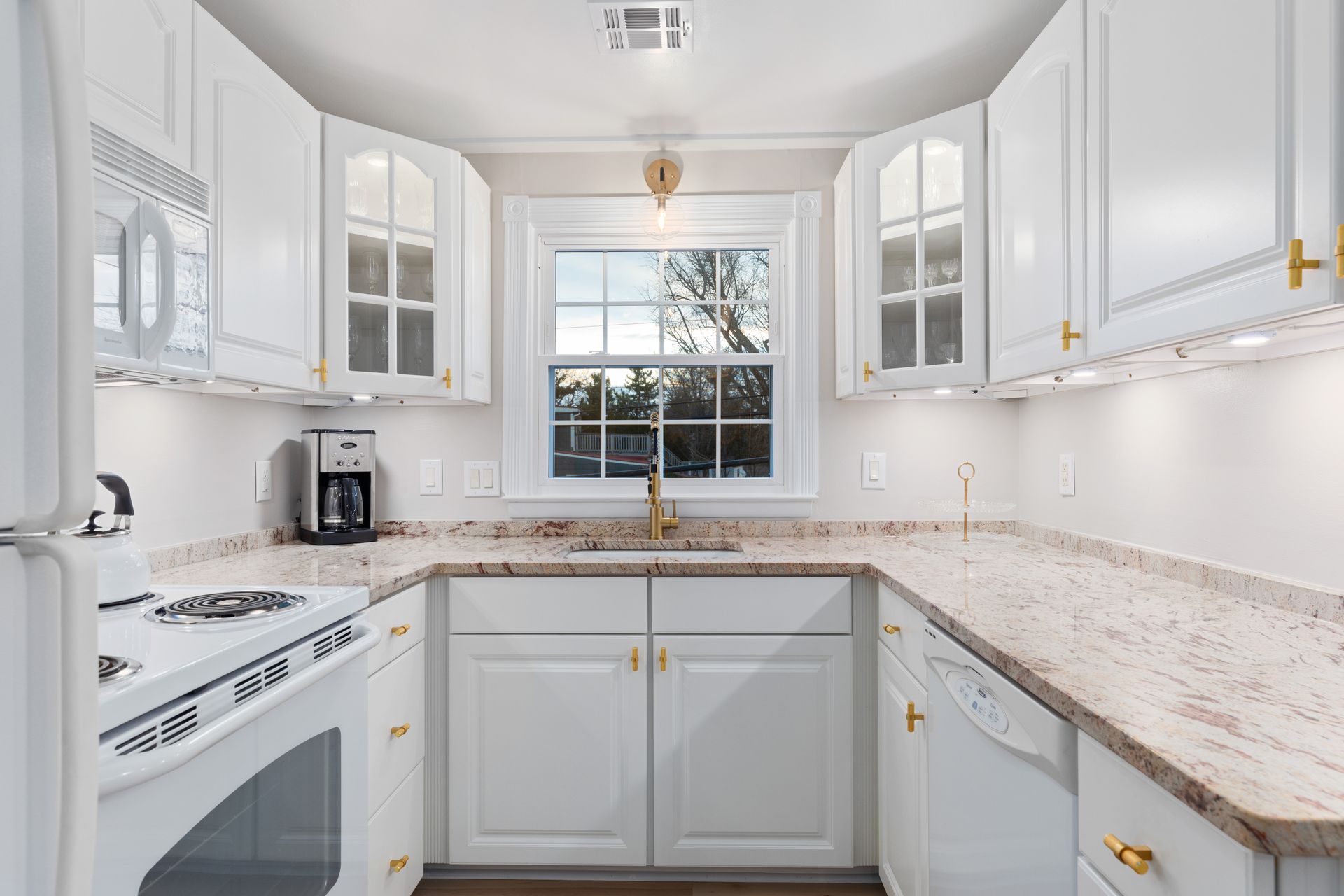 A kitchen with white cabinets , granite counter tops , a stove , dishwasher , and a window.